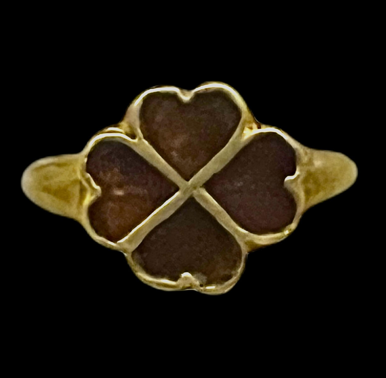 Gold four-leaf clover ring with dark gemstone petals on a black background.